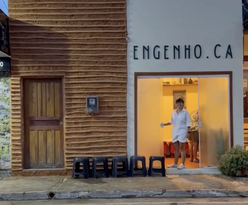 Fachada da Engenho.ca: parede de taipa, porta de madeira e o letreiro da marca sobre a vitrine iluminada